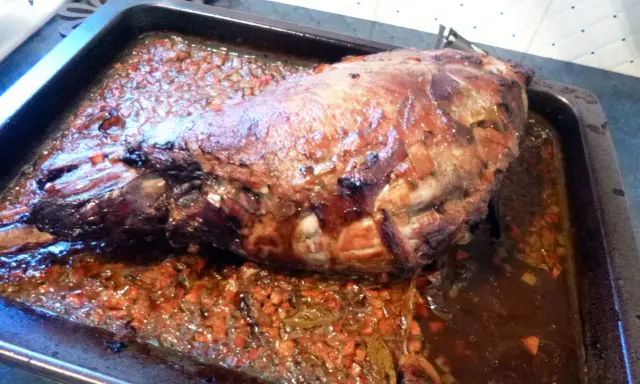 Gigot de sanglier rôti 7h, baignant dans son jus avec des légumes coupés. Un plat savoureux prêt à être dégusté.