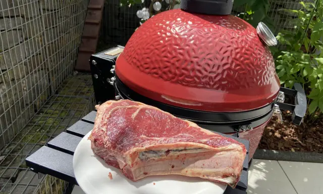 Une belle côte de bœuf crue attend sur une assiette blanche, prête à être grillée sur le barbecue rouge vif.