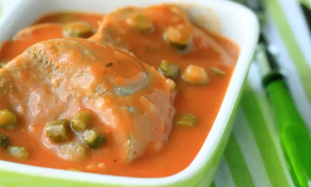 Tranches de langue de bœuf mijotées dans une sauce tomate onctueuse avec des petits pois. Un plat réconfortant servi dans un bol vert vif.