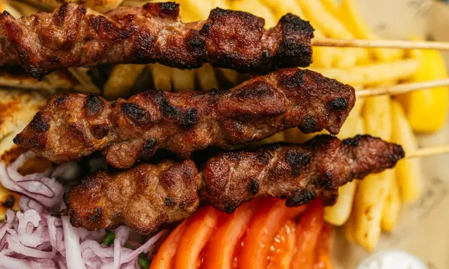 Brochettes de viande grillée, parfaites pour une cuisson indirecte au barbecue, accompagnées de frites, pain pita, tomates et oignons.