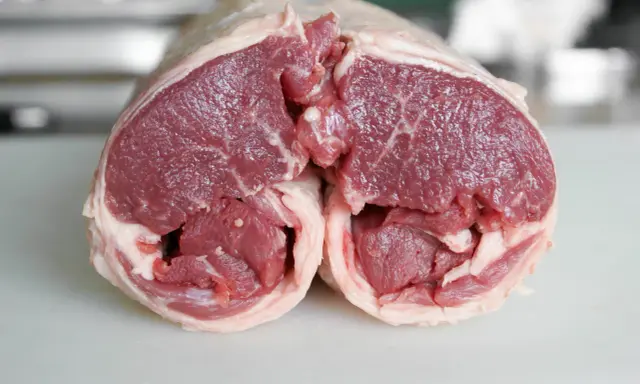 Un plat avec agneau cru, coupé en deux, révélant la chair rouge vif et le gras blanc. Prêt pour une cuisson savoureuse.