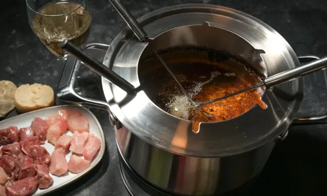 Préparation pour comment faire une fondue bourguignonne : morceaux de viande crue, pain et huile chaude dans le caquelon.