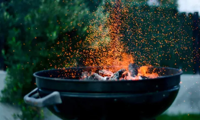 Un barbecue en plein air, avec des braises incandescentes et des étincelles qui dansent. L'odeur du barbecue bois ou charbon emplit l'air.