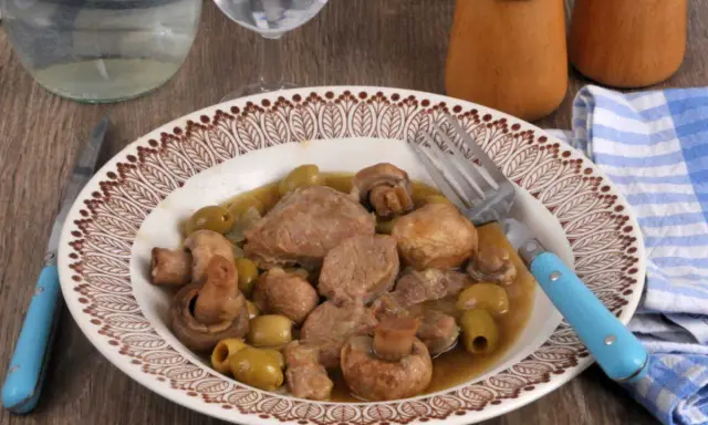 Un délicieux sauté de veau aux olives et champignons, servi dans une assiette décorée, prêt à être dégusté avec une fourchette bleue.