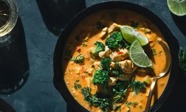 Un plat de poulet et brocolis baignant dans une sauce curry crémeuse, garni de quartiers de citron vert et de persil frais. Un délice !