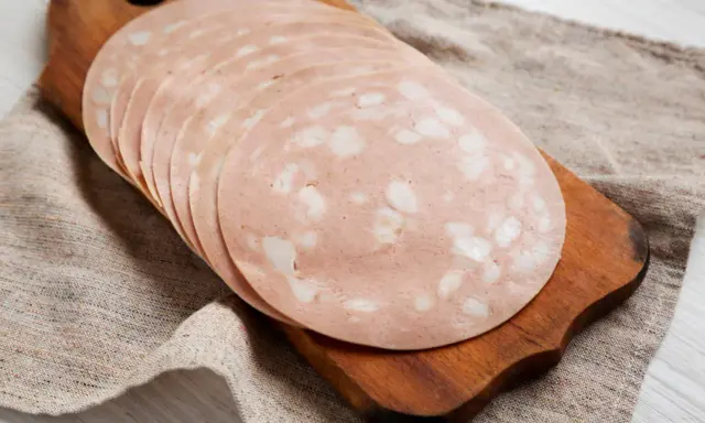 Tranches de mortadelle cuit ou cru, disposées en éventail sur une planche à découper en bois, sur un tissu de lin.