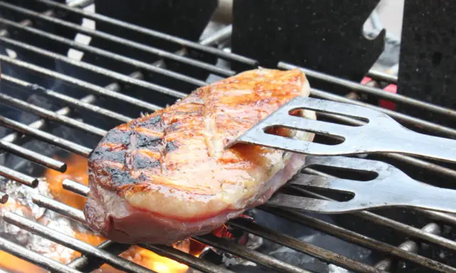 Magret de canard en cuisson indirecte sur un Weber, retourné avec une spatule. La peau est grillée et dorée, la chair rosée.