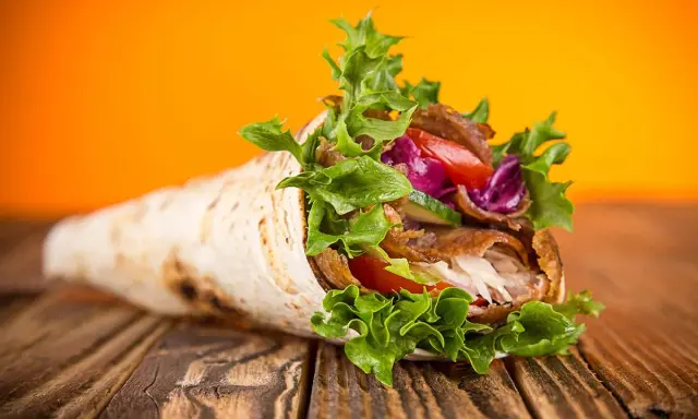 Un délicieux kebab maison garni de viande, salade croquante, tomates et chou rouge, sur un fond orange vif.