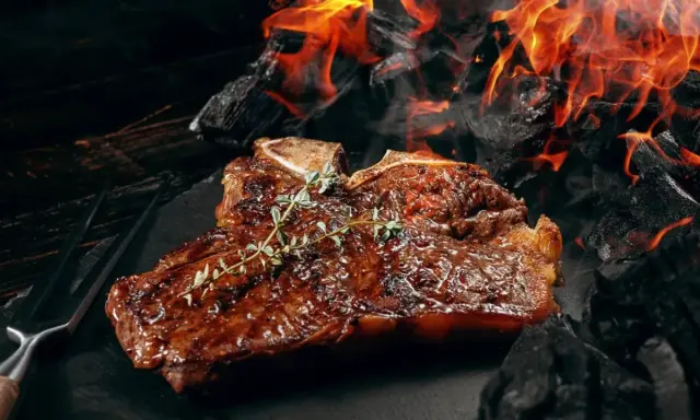 Un steak T-bone juteux, garni de thym, cuit sur des braises ardentes. Une parfaite recette barbecue pour les amateurs de viande.