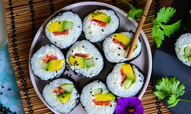 Assiette de makis frais, parfaits pour une recette sushi maison. Avocat, saumon et concombre roulés dans du riz et des algues, parsemés de graines de sésame.