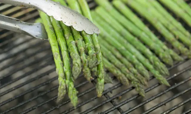 Des asperges vertes grillées, parfaites pour une recette simple et savoureuse. Les pinces saisissent un bouquet prêt à être retourné.