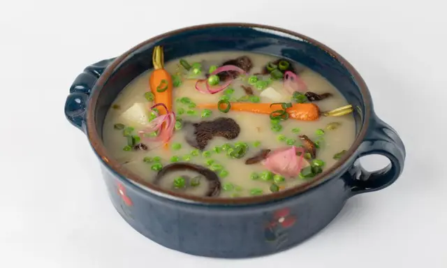 Délicieuse recette végétarienne : un potage crémeux aux carottes, petits pois, pommes de terre et champignons, garni d'oignons rouges et de ciboule.