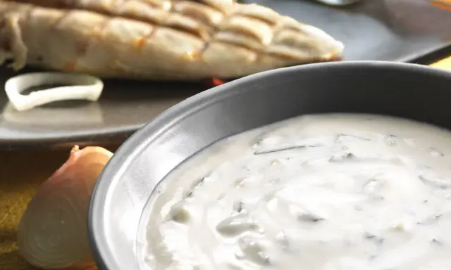 Sauce blanche crémeuse avec herbes, peut-être une différence sauce tartare et béarnaise. Poisson grillé en arrière-plan.