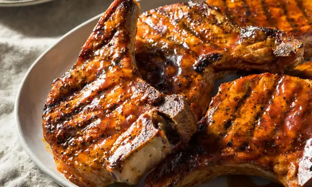 Trois côtes de porc barbecue, grillées et nappées d'une sauce savoureuse, sur une assiette blanche.