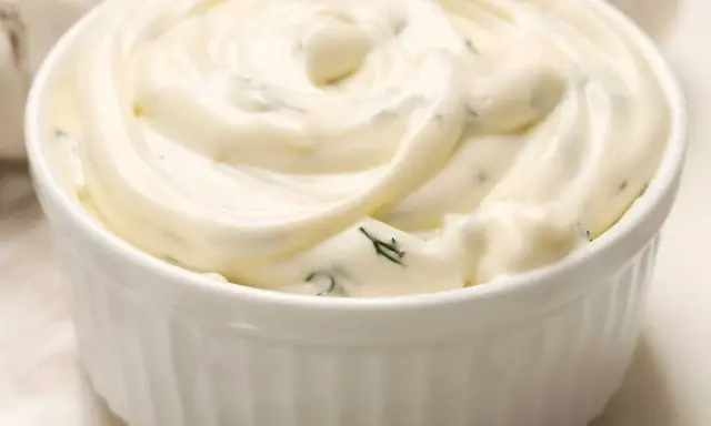 Un bol blanc rempli de sauce césar crémeuse, parsemée d'herbes vertes. Parfait pour accompagner une salade.
