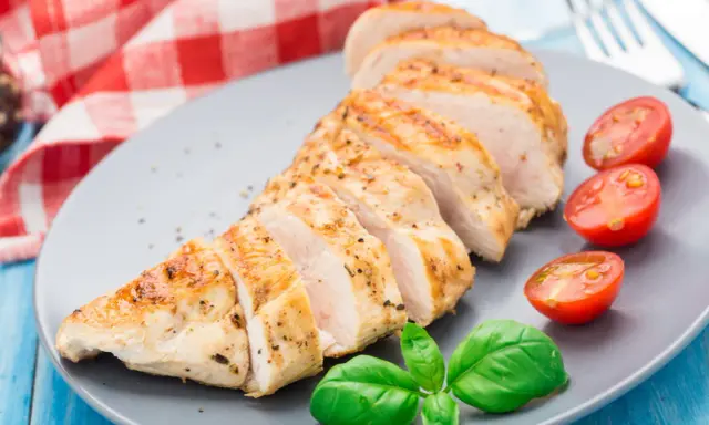 Un délicieux filet de poulet grillé, tranché et servi avec des tomates cerises et du basilic frais sur une assiette grise.