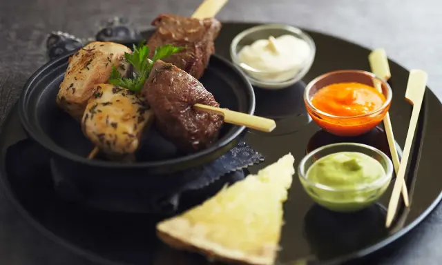 Brochettes de poulet et de bœuf, accompagnées de différentes sauces : mayonnaise, sauce tomate épicée et sauce verte.