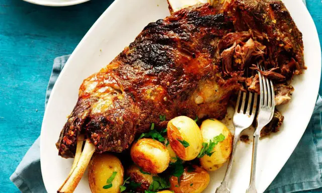Épaule d'agneau rôtie, servie avec des pommes de terre et du persil. Le temps de cuisson de l'épaule d'agneau au barbecue Weber est parfait pour cette viande tendre.