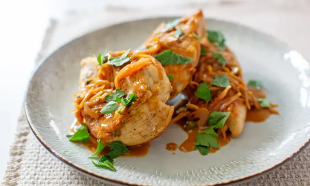 Trois escalopes de poulet nappées d'une sauce onctueuse aux oignons caramélisés et garnies de persil frais. Un plat savoureux et réconfortant.