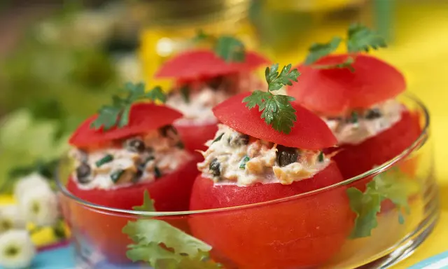 Tomates farcies froides aux légumes, garnies de persil frais, présentées dans un bol en verre. Un délice estival.
