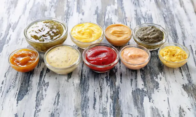 Neuf coupelles de sauces variées, dont le ketchup, la moutarde et des sauces vertes et orangées. Ces sauces sont parmi les 10 sauces les plus utilisées.
