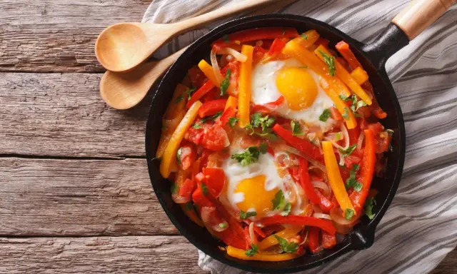 Poêlée de poivrons, tomates et œufs, une recette de piperade savoureuse, garnie de persil frais.