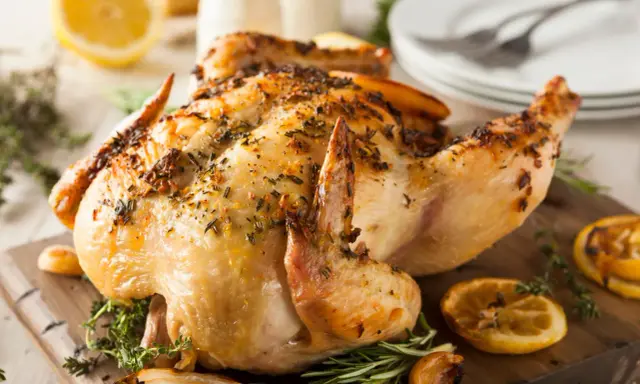 Un délicieux poulet rôti, doré et parfumé aux herbes, est servi sur une planche en bois avec des quartiers de citron et de l'ail rôti.