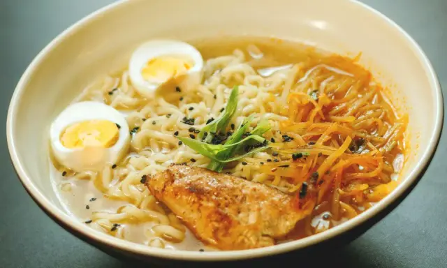 Un bol de ramen poulet avec nouilles, œuf dur, poulet grillé, julienne de carottes et oignons verts. Une recette réconfortante.