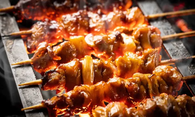 Brochettes de bœuf et fromage grillées sur des braises ardentes, dégageant une fumée alléchante.