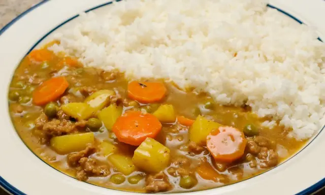 Un plat de riz blanc servi avec un curry japonais savoureux, garni de morceaux de carottes, de pommes de terre et de petits pois.