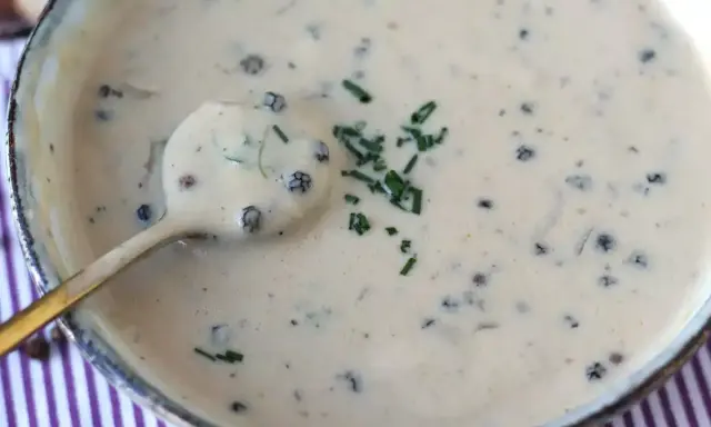 Une cuillère dorée plonge dans une onctueuse sauce au poivre, garnie de ciboulette fraîche.
