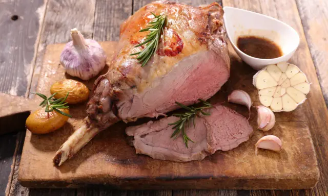 Gigot d'agneau rôti, servi avec des pommes de terre, de l'ail et une sauce. Une recette gastronomique qui met l'eau à la bouche.