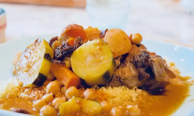 Un plat généreux de couscous algérien, garni de légumes tendres, de pois chiches et de morceaux de viande savoureux, le tout nappé d'une sauce parfumée.