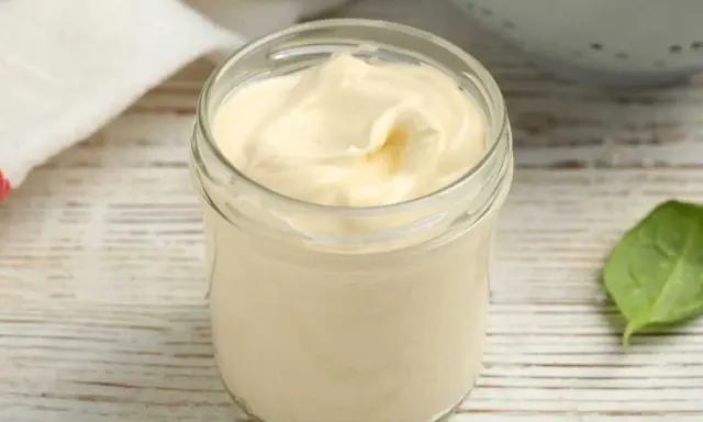 Un pot de mayonnaise sans huile, crémeuse et onctueuse, sur une table en bois. Une feuille verte à côté.
