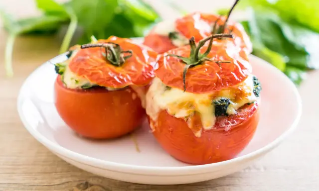 Trois tomates farcies au fromage fondant et aux herbes, servies sur une assiette blanche.