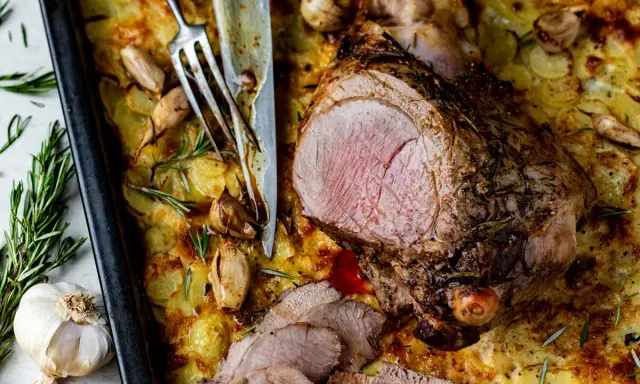 Un gigot d'agneau rôti, tranché, servi sur un lit de pommes de terre gratinées avec de l'ail et du romarin.