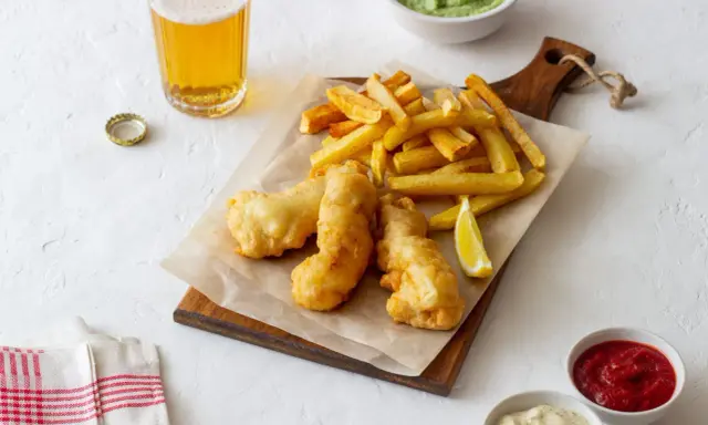Un plat de fish and chips croustillant, servi avec des frites dorées, un quartier de citron, et des sauces. Une bière blonde complète ce repas.