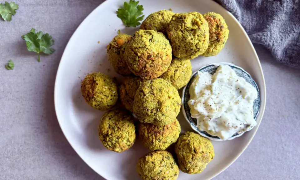 Assiette de falafels dorés, prêts à être dégustés. Une recette facile pour un plaisir garanti. Sauce blanche et coriandre pour accompagner.