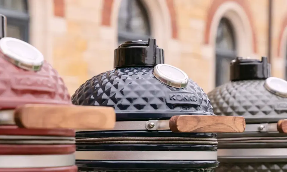 Trois barbecues kamado de couleurs différentes, prêts pour un avis. Le noir est au centre, le rouge à gauche, le gris à droite.