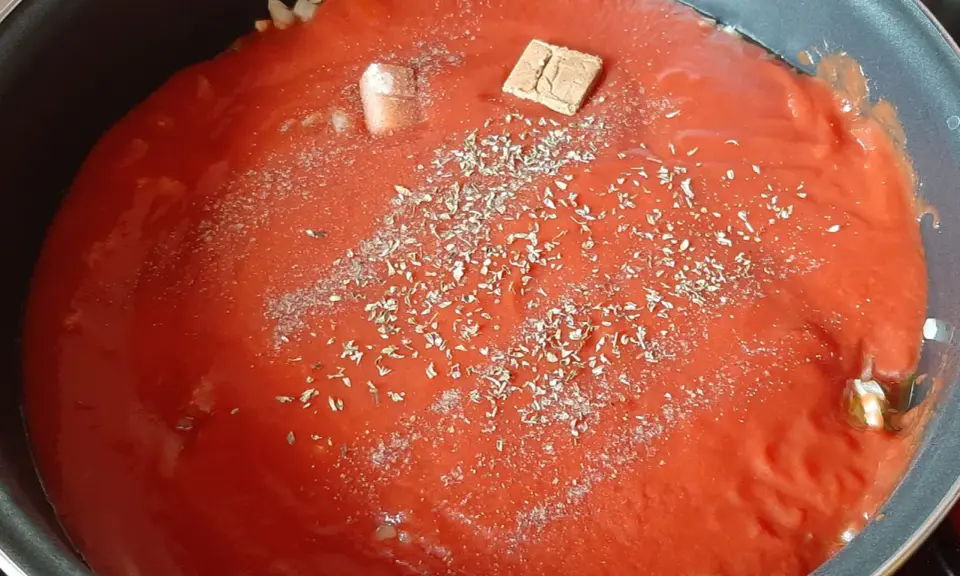 Sauce tomate maison mijote dans une poêle, agrémentée d'herbes et d'un cube de bouillon.