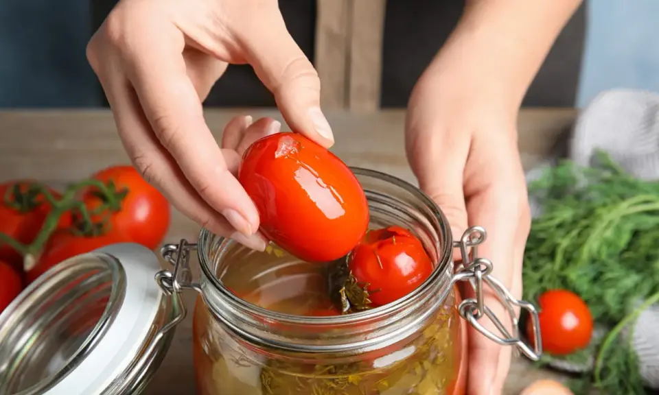 Mains ajoutant une tomate dans un bocal pour une recette de tomate farcie le parfait.
