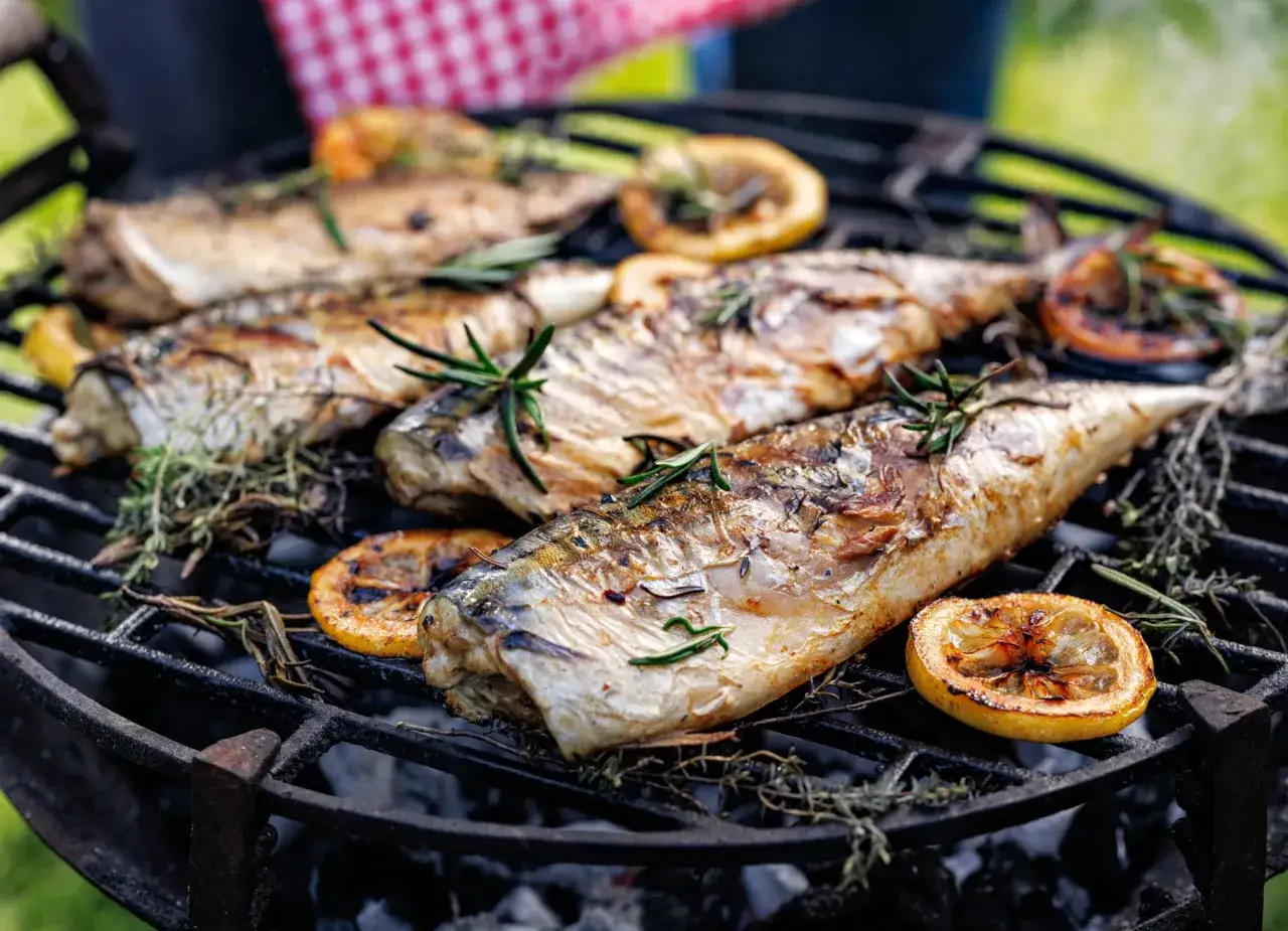 Plusieurs merlus grillés sur un barbecue, ornés de romarin et de rondelles de citron caramélisées. Un délice estival !