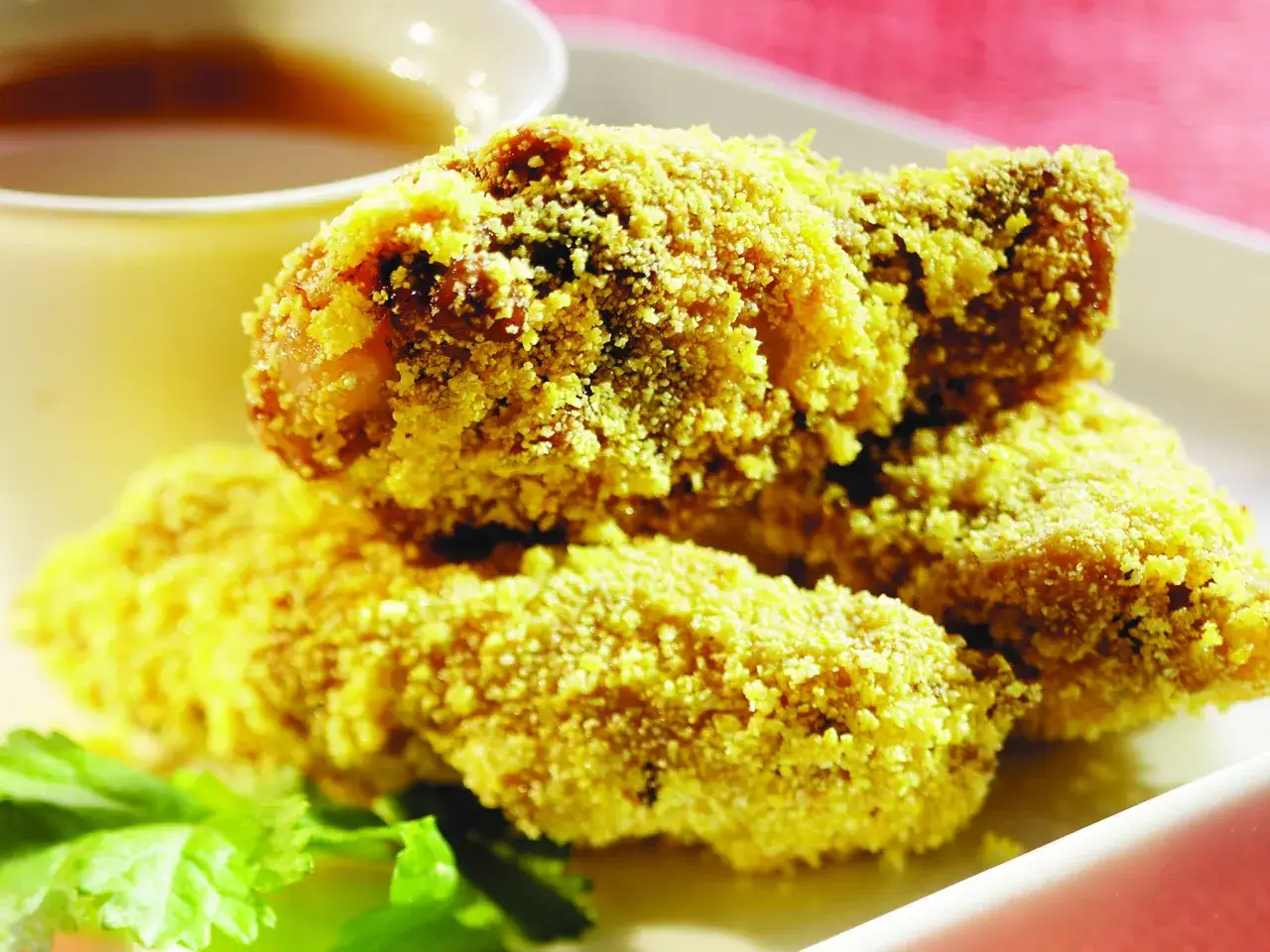Trois chicken lollipops dorés et croustillants, servis avec une sauce dans un bol.