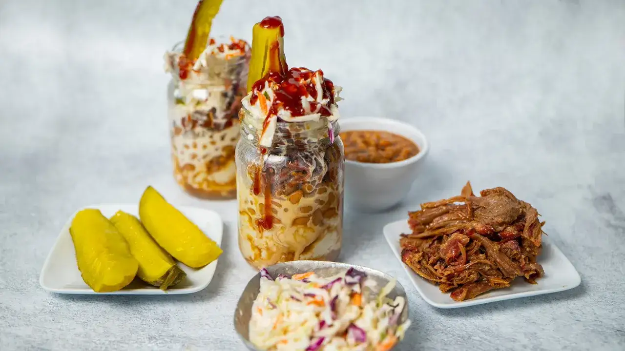 Un délice de pulled pork servi en pot avec salade de chou, haricots et cornichons.