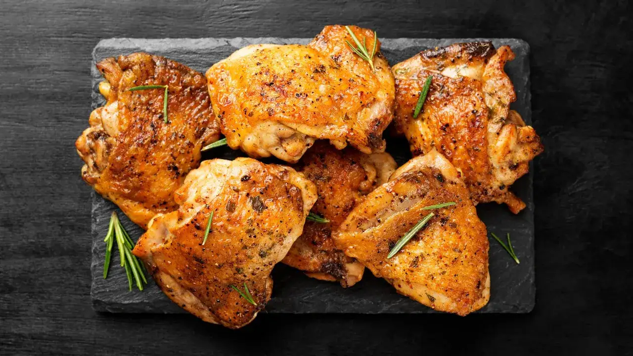 Un assortiment de cuisse poulet désossée, dorées et savoureuses, garnies de romarin frais sur une planche d'ardoise.