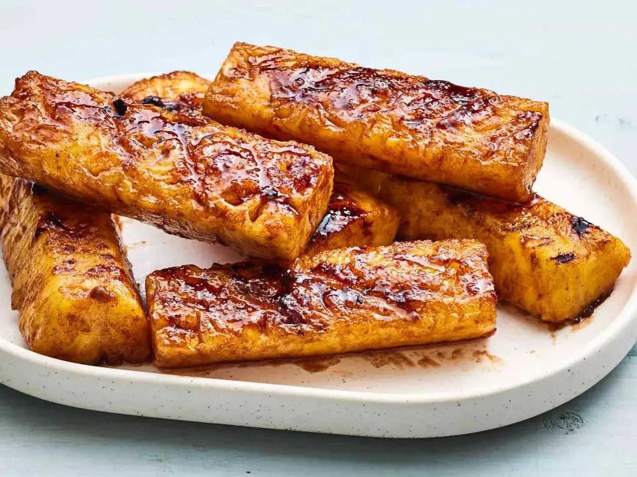 Des morceaux d'ananas caramélisés à la plancha, brillants et appétissants, disposés sur une assiette blanche.