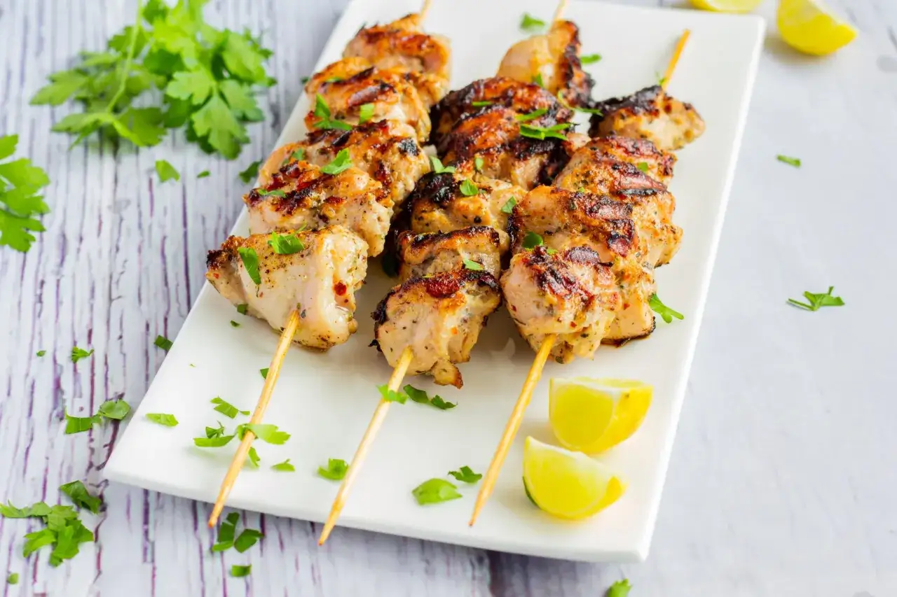 Brochettes de poulet citron grillé, garnies de persil frais et accompagnées de quartiers de citron vert. Un délice estival !