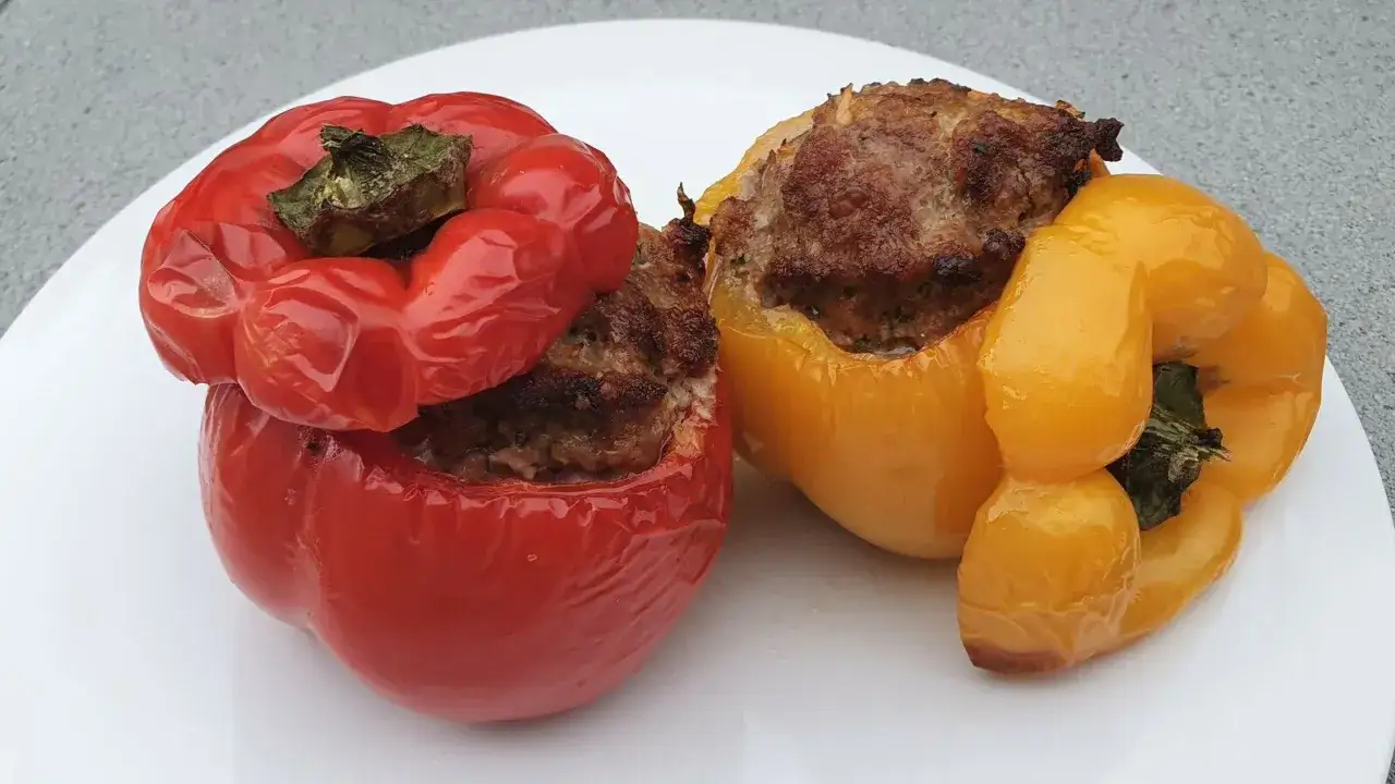 Deux poivrons farcis, un rouge et un jaune, sont présentés sur une assiette blanche. La garniture savoureuse déborde des légumes cuits.