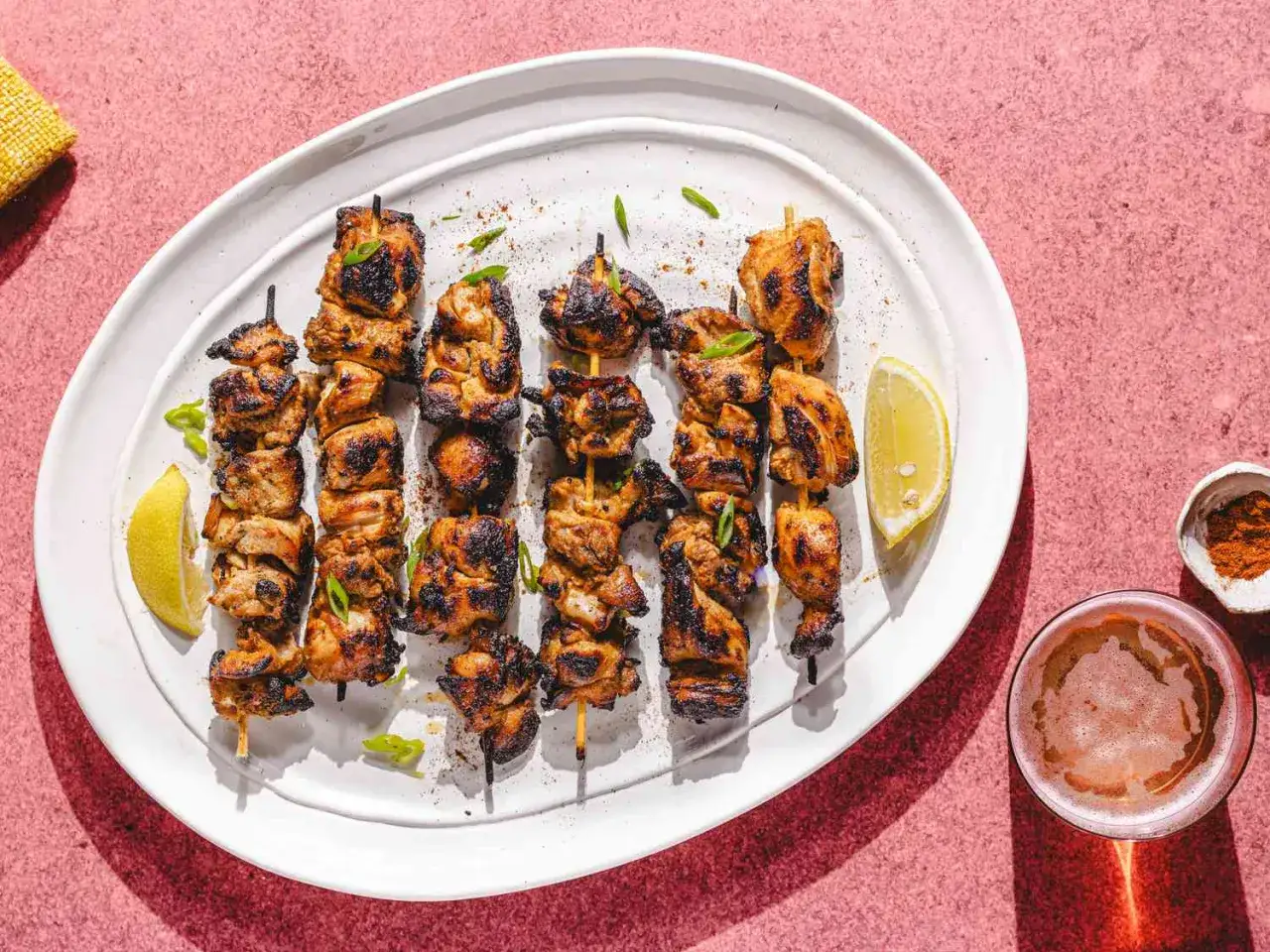 Brochettes de poulet tikka grillé, garnies de ciboule et de quartiers de citron, servies avec une bière et des épices.