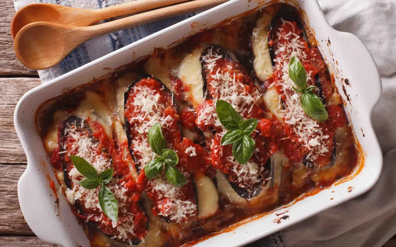 Un plat d'aubergine parmigiana gratiné, garni de basilic frais et de parmesan râpé, prêt à être dégusté.